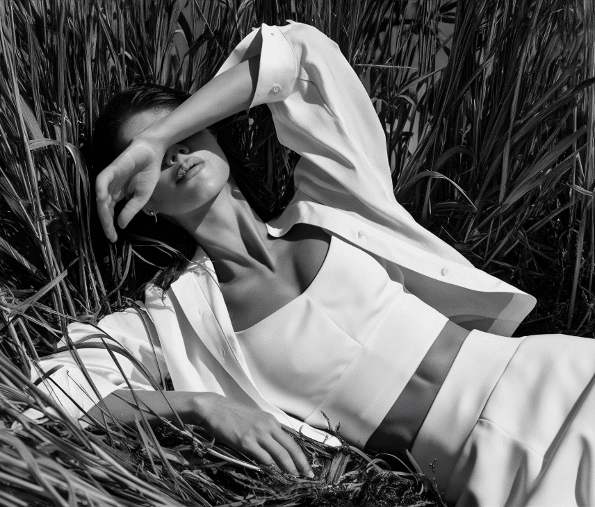 Fifteen Twelve Beauty woman laying in tall grass, wearing an oversized white blouse and the white top and jeans beneath